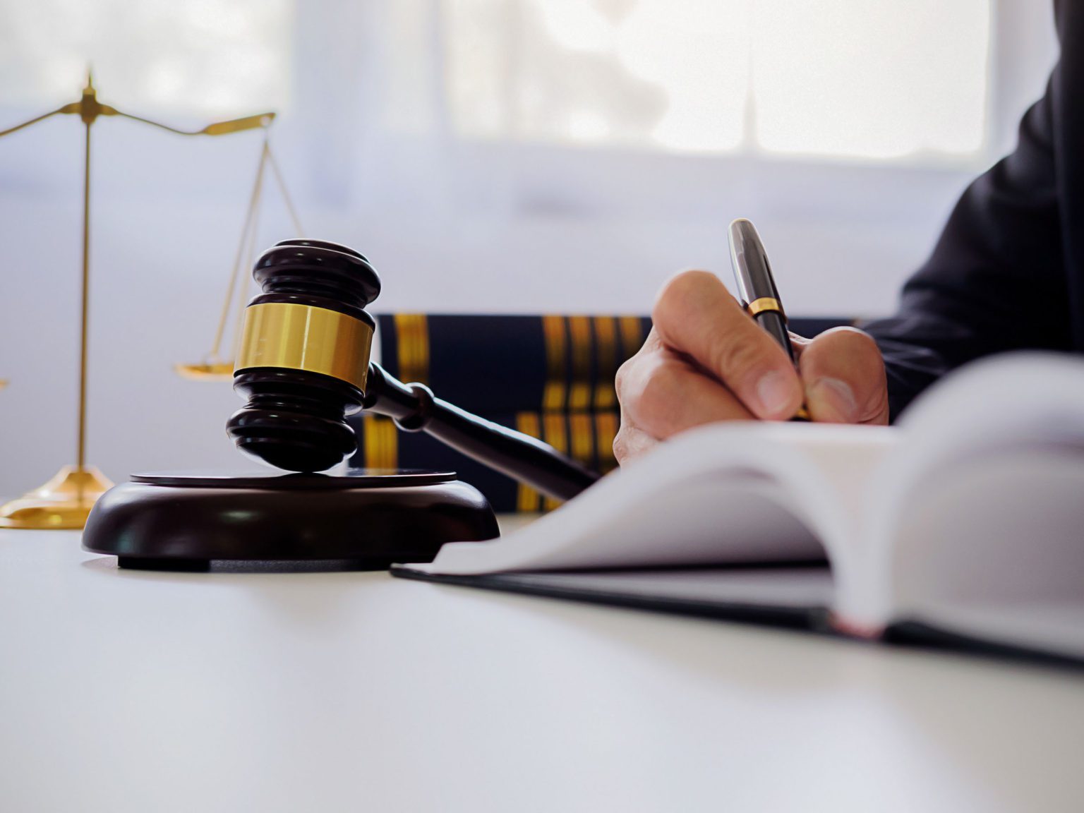 An image of a hand holding a gavel and signing a document, representing the concept of law and justice